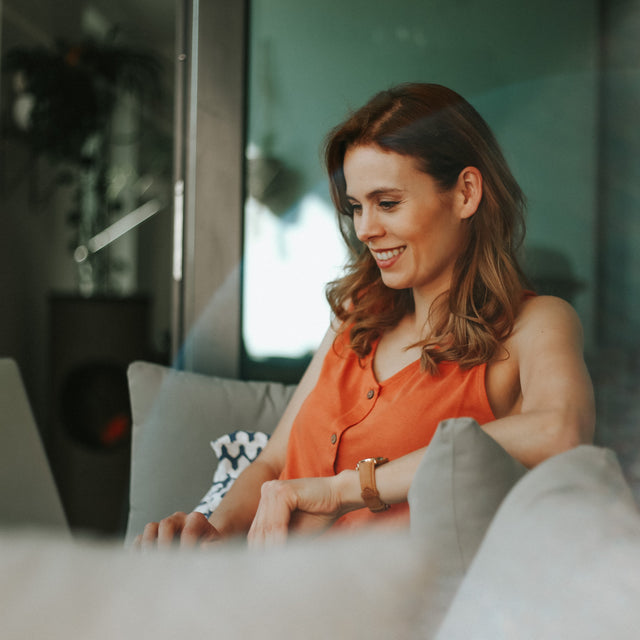 Women in orange top smiling and looking at laptop
