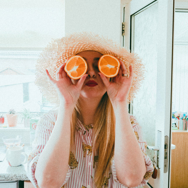 A woman being goofy and holding an orange cut in half up to her eyes. She feels confident after her routine STI testing.