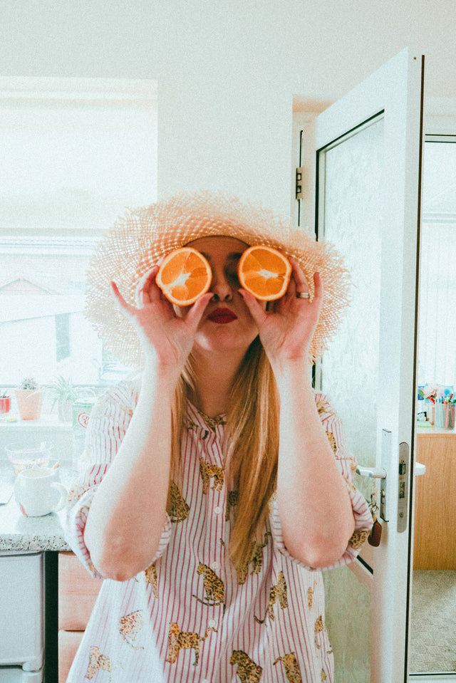 A woman being goofy and holding an orange cut in half up to her eyes. She feels confident after her routine STI testing.