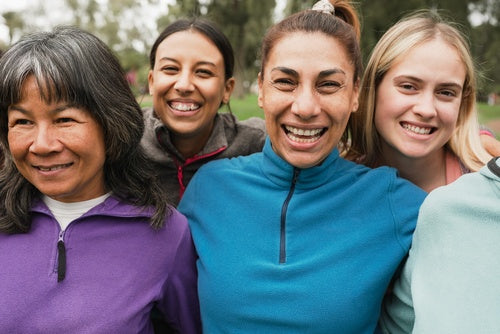 Four women of different ages and backgrounds smile together outdoors in colorful fleece pullovers.