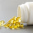 Golden softgel capsules spill from a tipped white supplement bottle onto a gray surface.